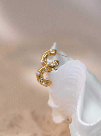 Gold crescent-shaped hoop earrings adorned with small white pearls, displayed on a white clam shell against a soft beige background.
