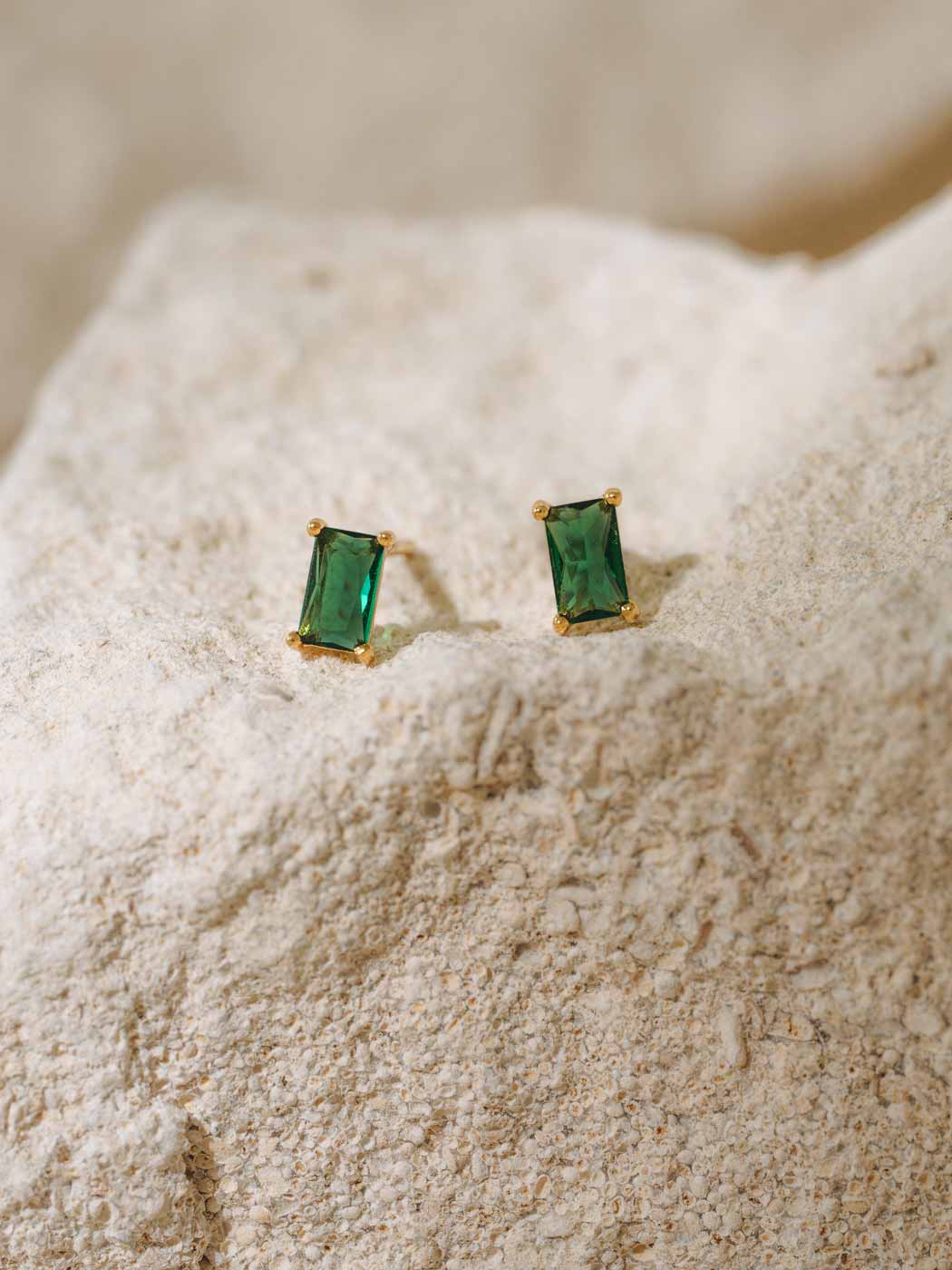 Pair of emerald green stud earrings on a textured beige surface