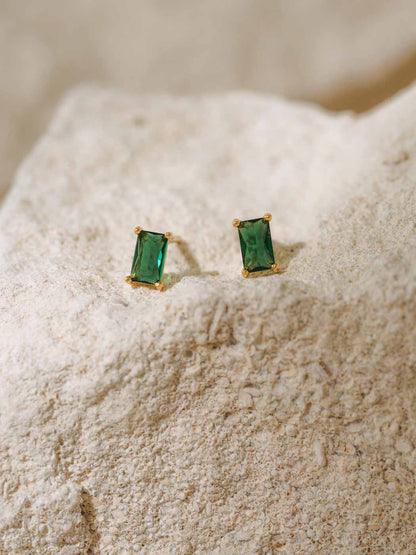 Pair of emerald green stud earrings on a textured beige surface