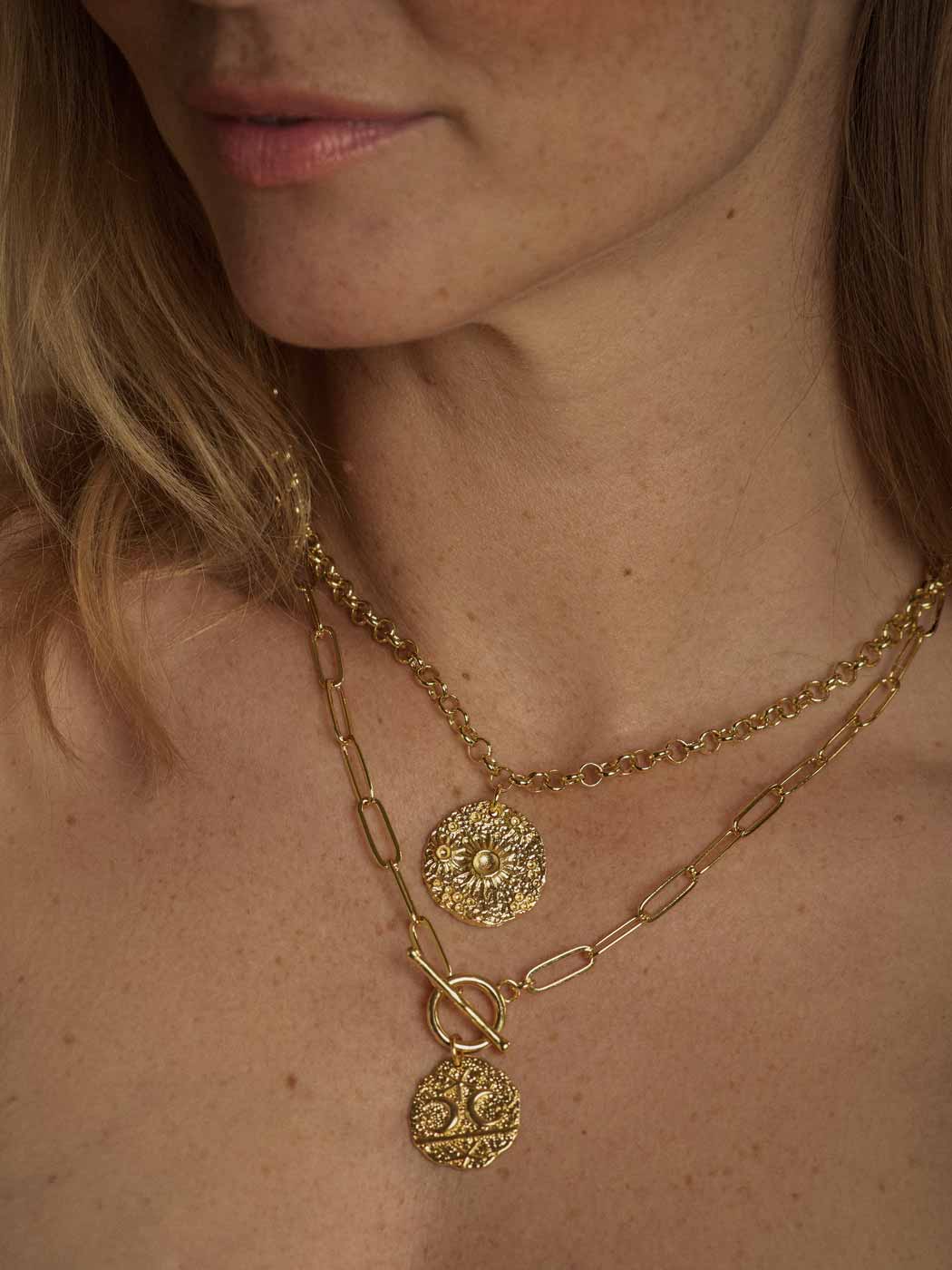 Close-up of a model wearing a layered gold necklace set with a paperclip chain, a chain link chain, and two round tree-of-life pendants.