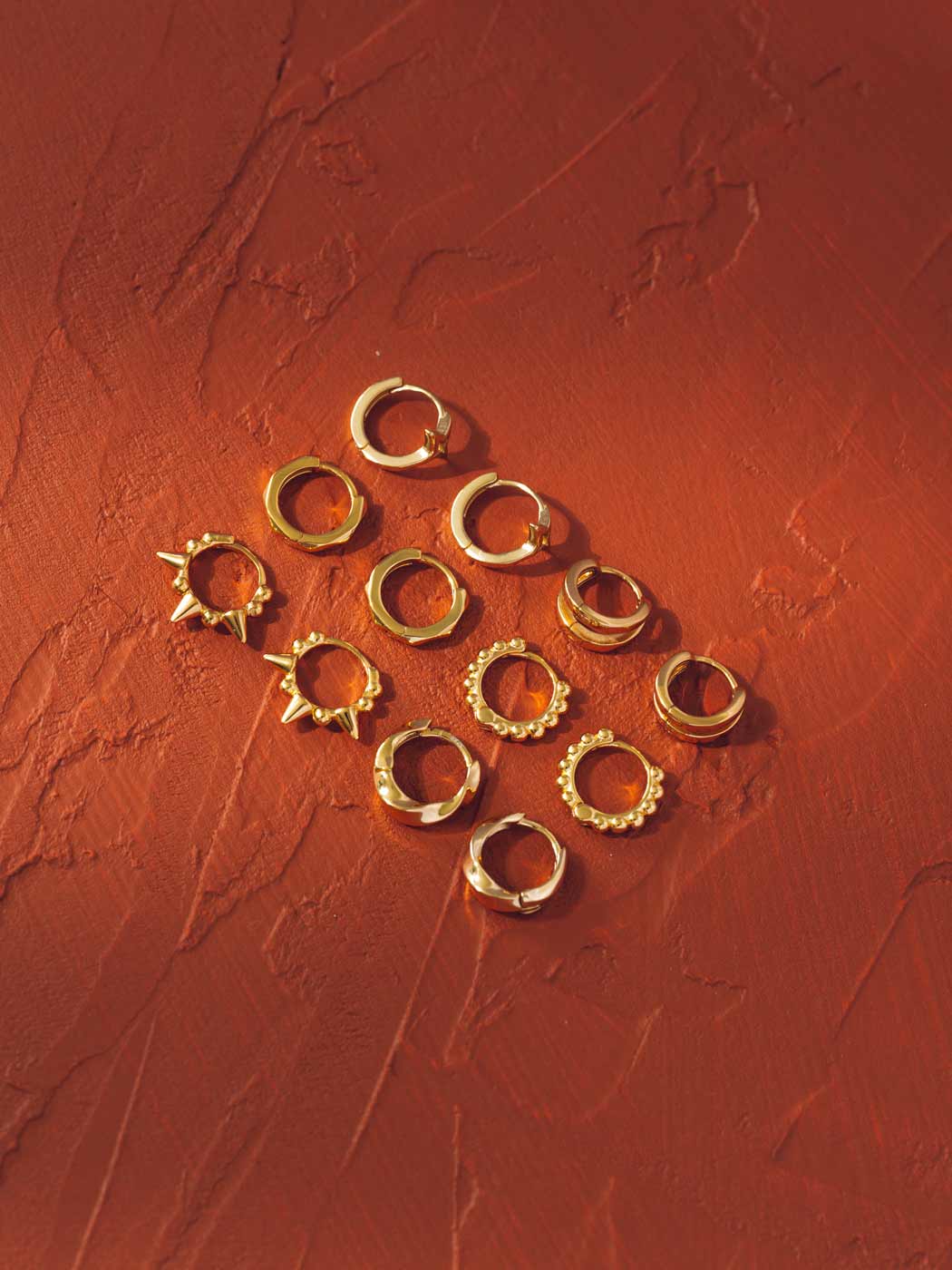 Gold hoop huggie earrings on a textured red surface