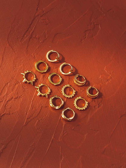 Gold hoop huggie earrings on a textured red surface