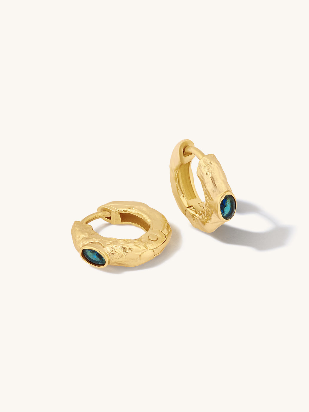A pair of textured gold huggie hoop earrings with small oval dark green cabochon accents, displayed on a clean off-white background.
