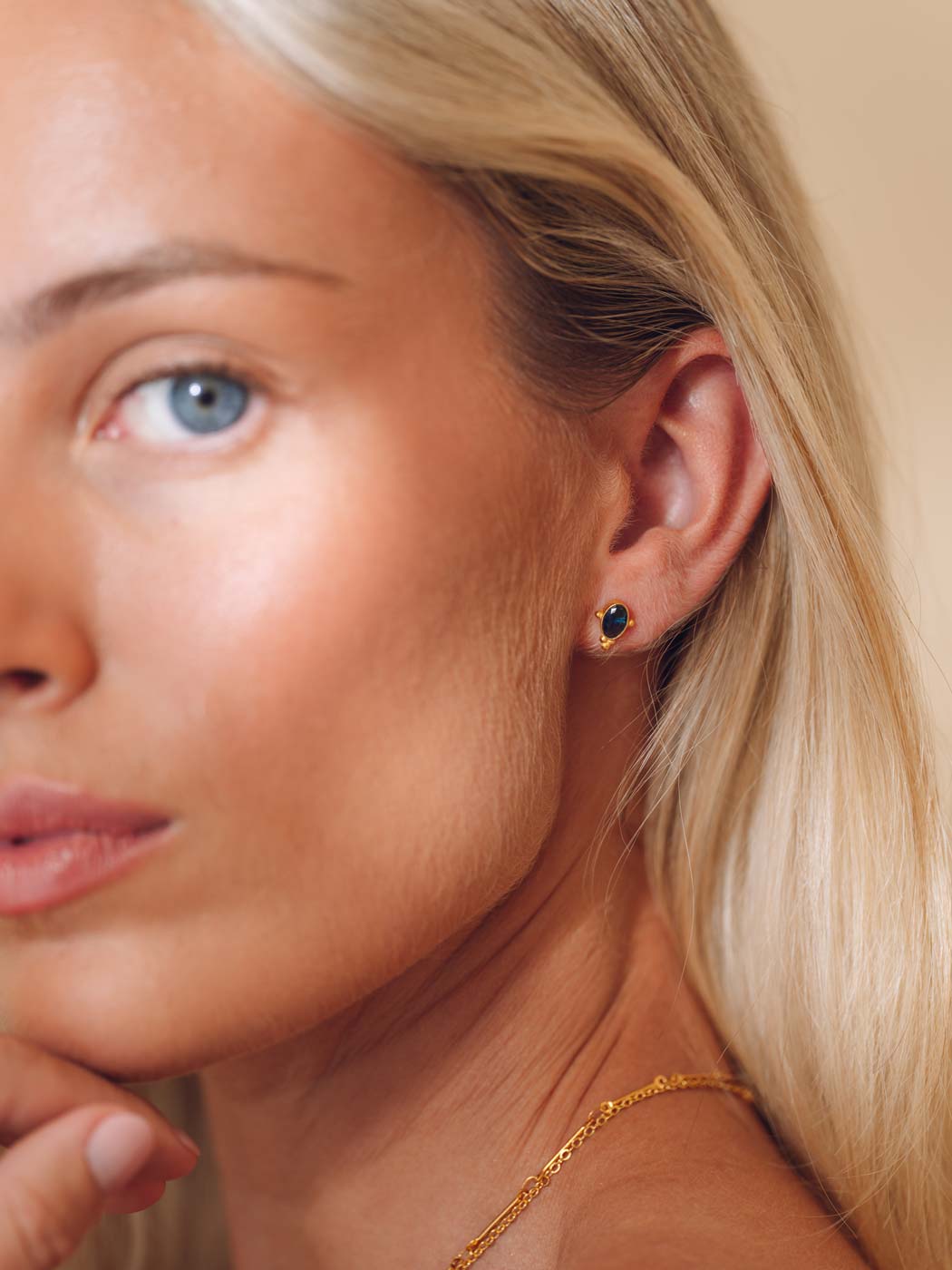 Close-up of a woman wearing gold sapphire bohemian stud earrings with a sapphire stone
