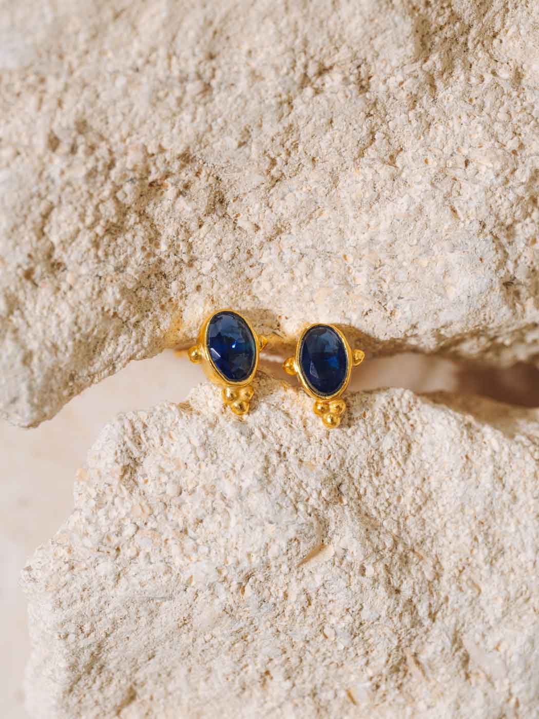 Gold earrings with blue sapphire stones on textured rocks