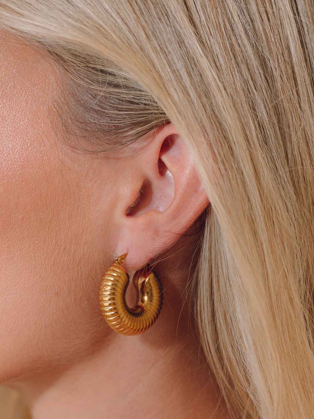 Chunky statement gold hoop earring worn by a person with blonde hair.