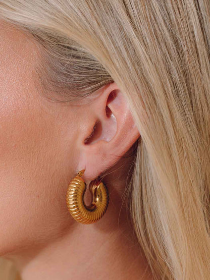 Chunky statement gold hoop earring worn by a person with blonde hair.