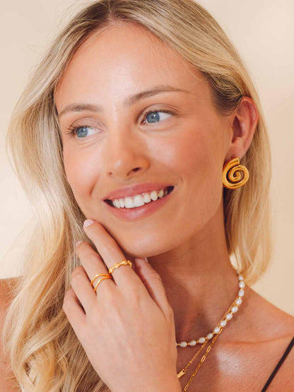 Woman wearing gold earrings, rings, and a necklace on a beige background