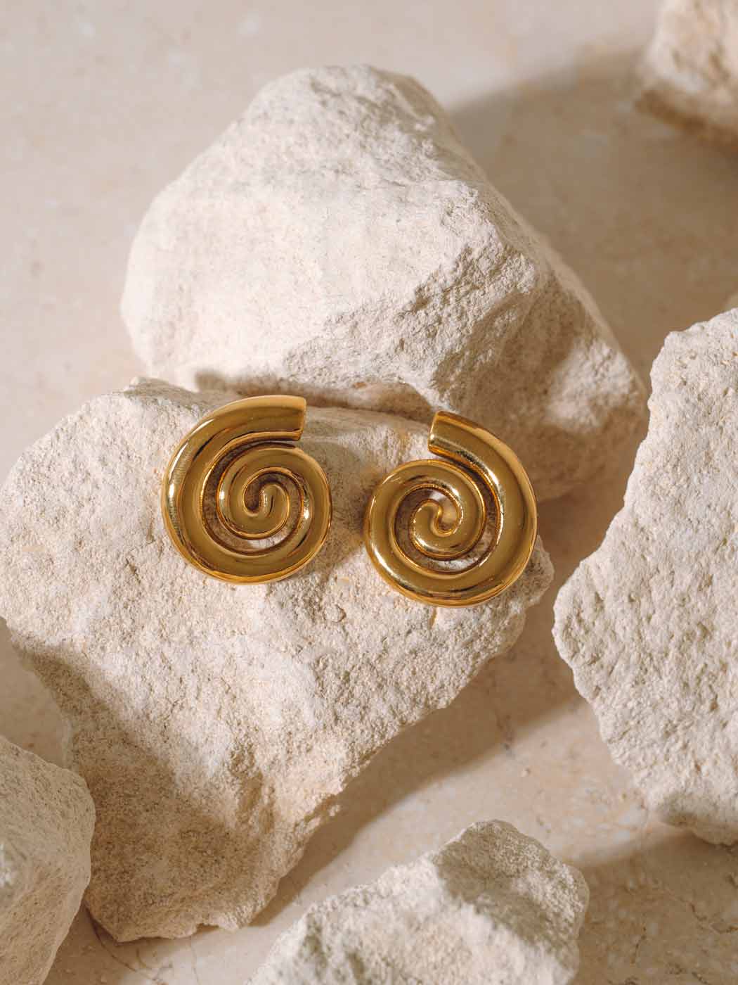 statement gold swirl stud drop earrings on rocks