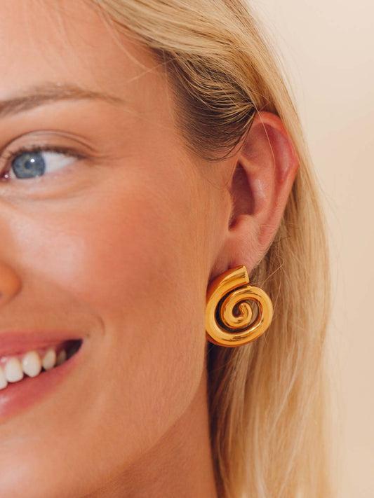 Close-up of a woman wearing gold spiral earrings on a beige background