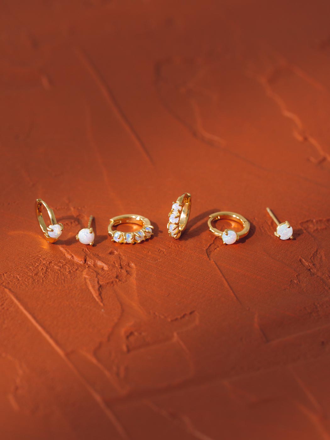 Set of gold and opal earrings on a textured red surface