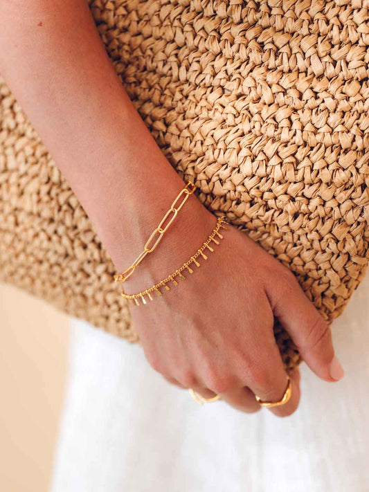 Gold bracelets and ring on a hand with a straw bag in the background