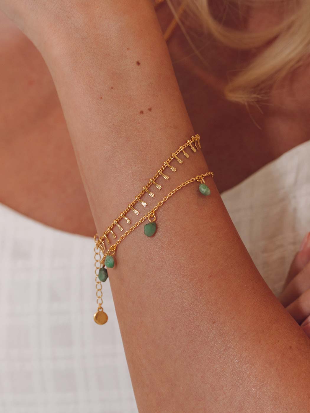 Gold boho bracelets with green beads on a person's wrist against a neutral background