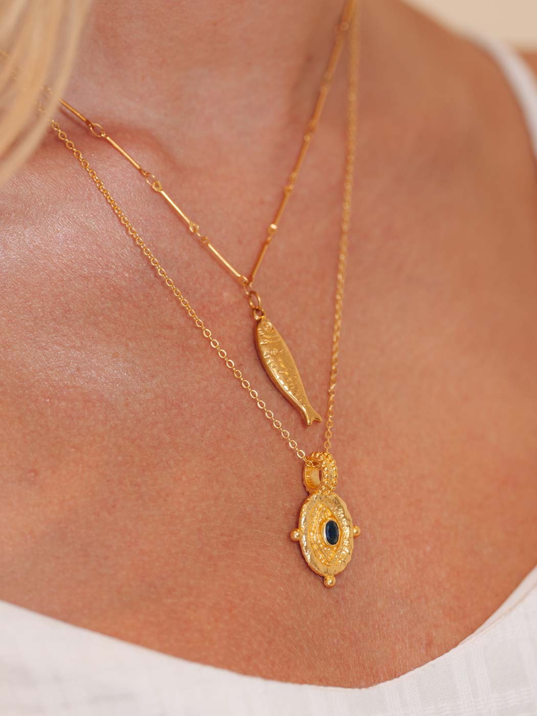 Gold necklace with a fish shaped pendant on a person wearing a white top.