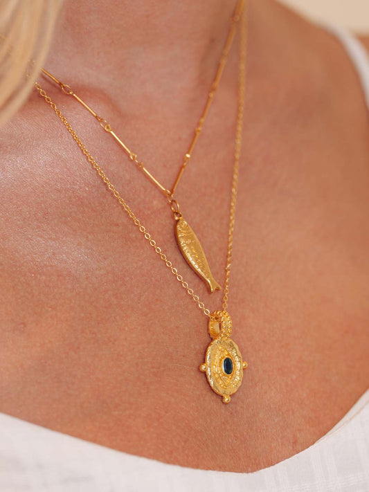 Gold necklace with a fish shaped pendant on a person wearing a white top.