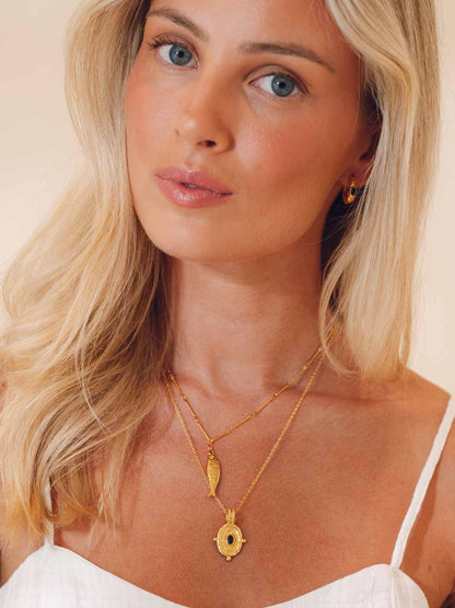 Woman wearing gold necklaces and earrings against a plain background