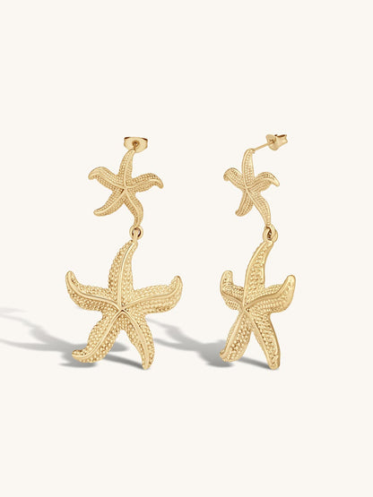 Gold statement starfish drop earrings on a white background