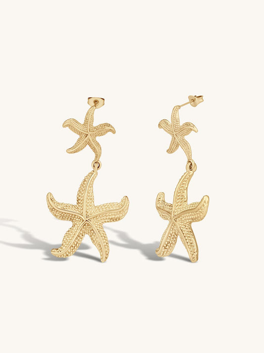 Gold statement starfish drop earrings on a white background