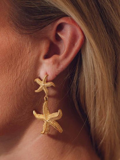 Gold statement starfish earrings worn by a person with blonde hair.