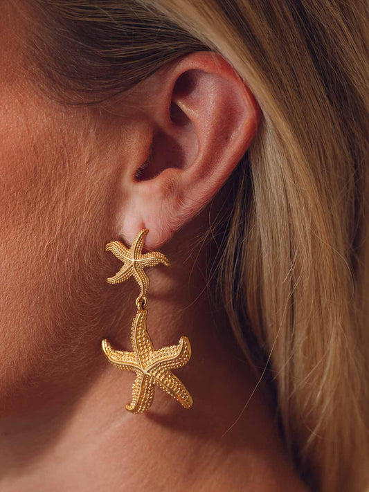 Gold statement starfish earrings worn by a person with blonde hair.
