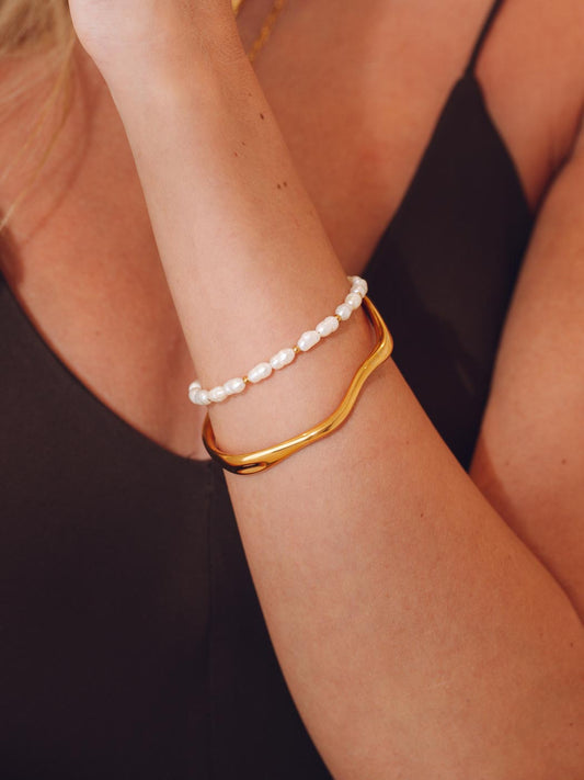 Gold bracelet and pearl bracelet on a person's wrist against a black background
