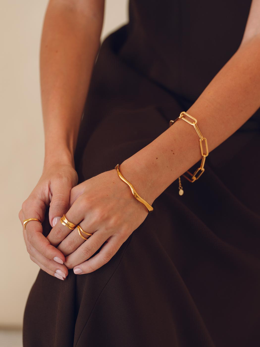 Close-up of a person's hands wearing gold bracelets and rings on a plain background
