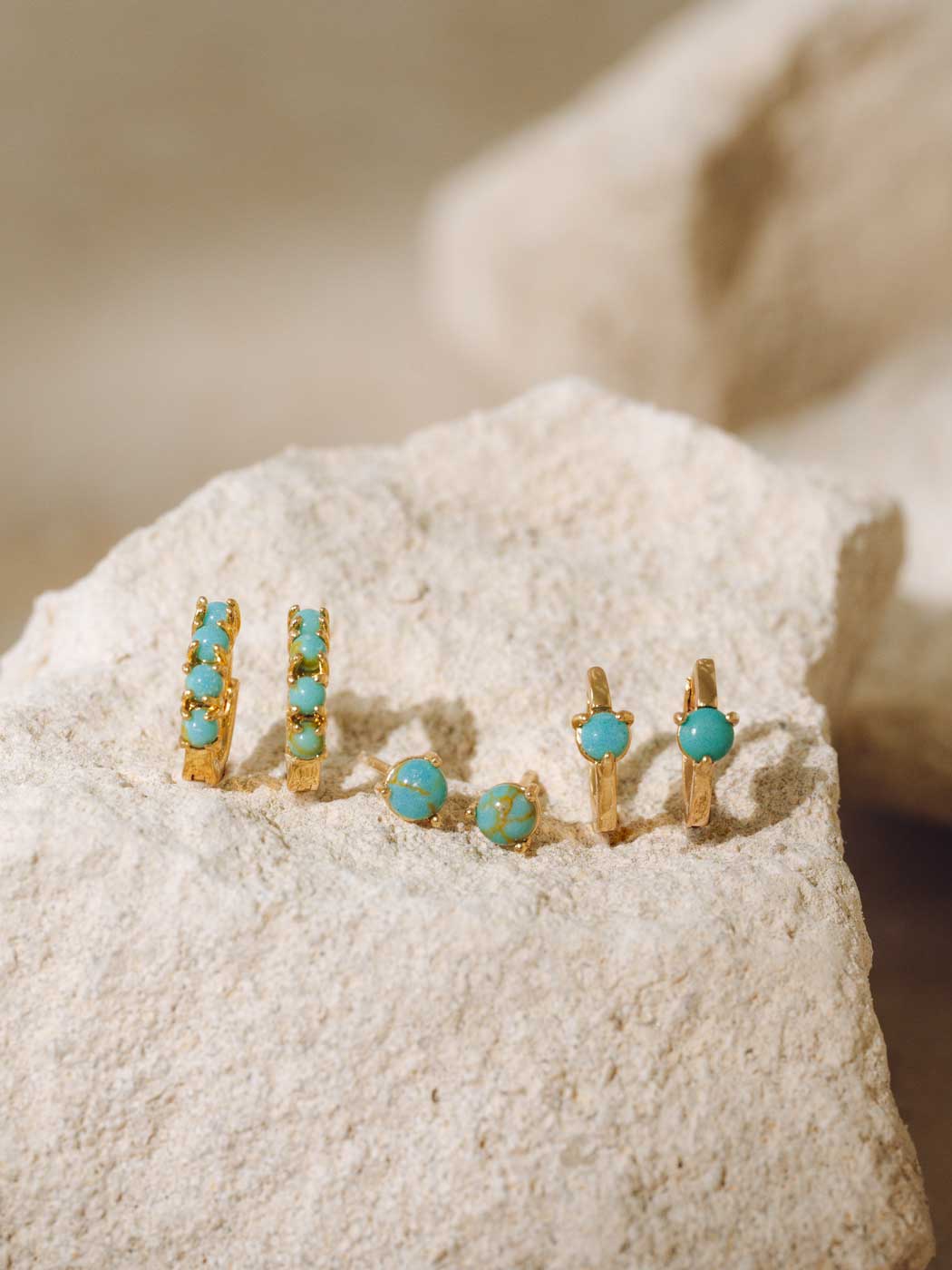 Gold earrings with turquoise stones on a textured surface
