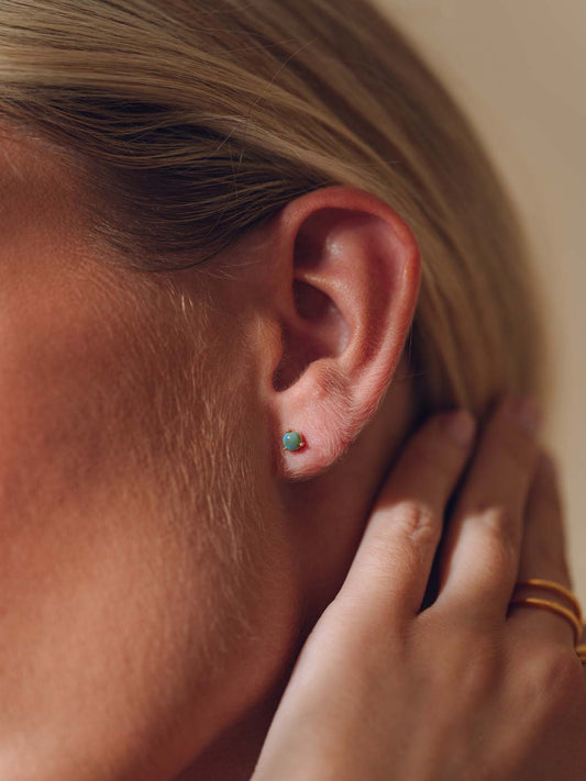 Close-up of an ear with gold stud earrings with a turquoise stone inlaid