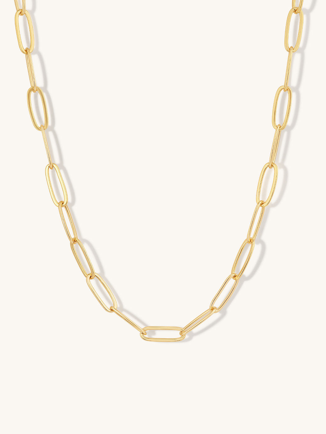 A gold paperclip chain necklace with elongated oval links, displayed against a clean off-white background.