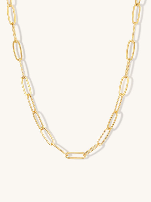 A gold paperclip chain necklace with elongated oval links, displayed against a clean off-white background.