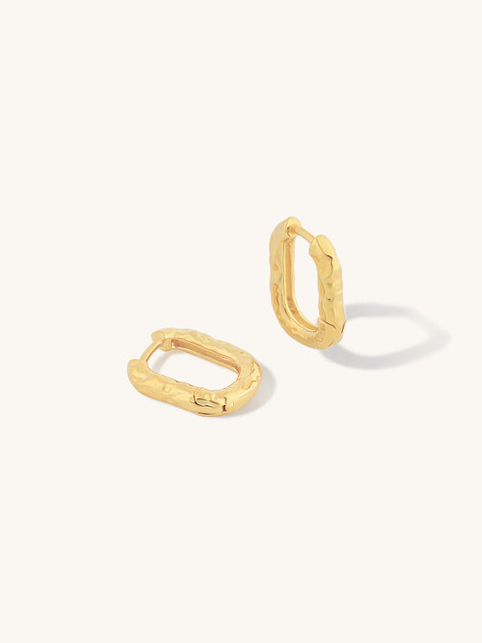 A pair of textured gold huggie hoop earrings on a clean, off-white background.