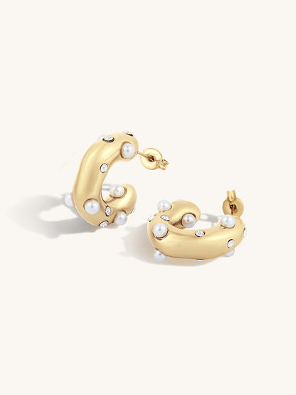 Gold crescent-shaped hoop earrings adorned with small white pearls and clear rhinestones, displayed on a clean off-white background.