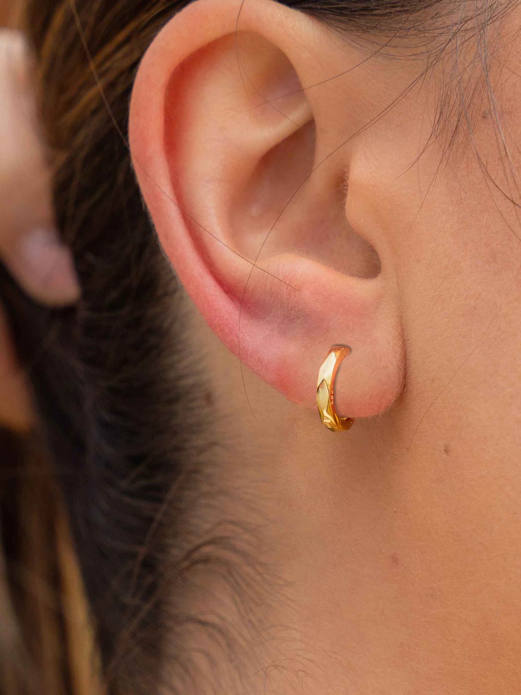 minimal faceted gold huggies on ear close up