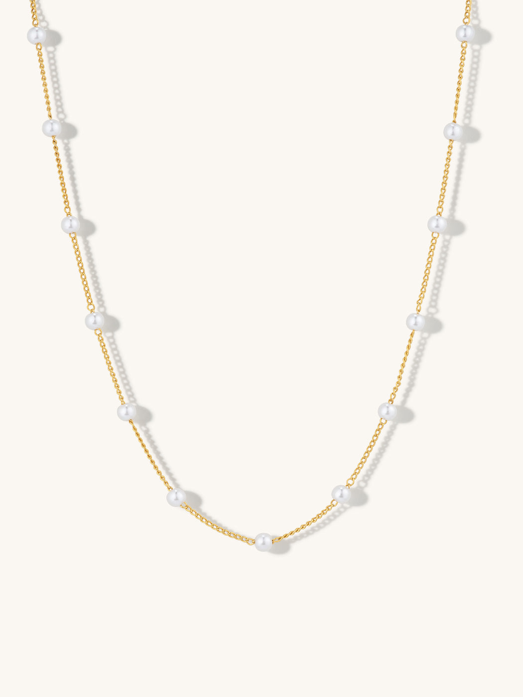 A delicate gold chain necklace featuring evenly spaced, small white pearl beads, displayed against a clean, off-white background.