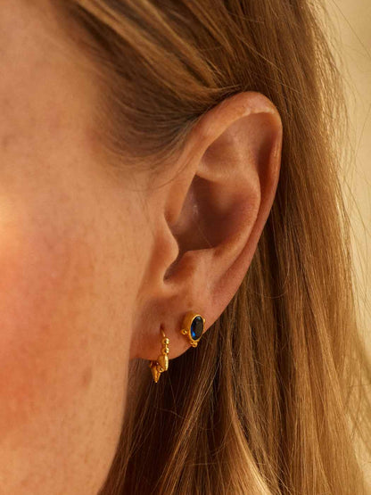 Close-up of an ear wearing gold earrings with a blue sapphire gemstone.