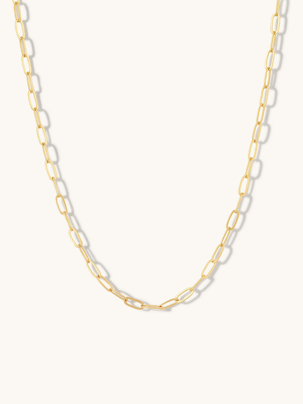 A gold paperclip chain necklace displayed against a clean, off-white background.
