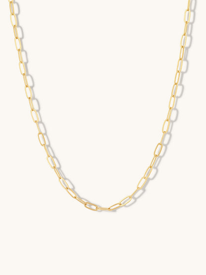 A gold paperclip chain necklace displayed against a clean, off-white background.