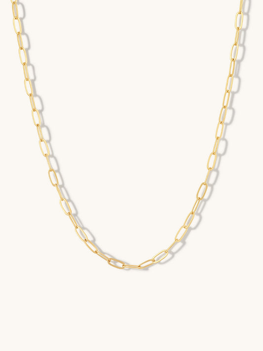 A gold paperclip chain necklace displayed against a clean, off-white background.