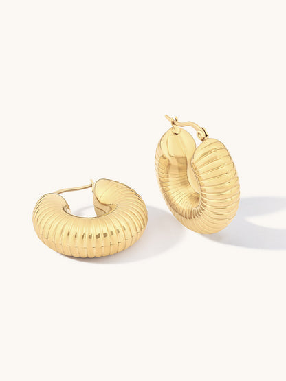 A pair of gold hoop earrings with a ribbed, textured finish, displayed on a clean off-white background.