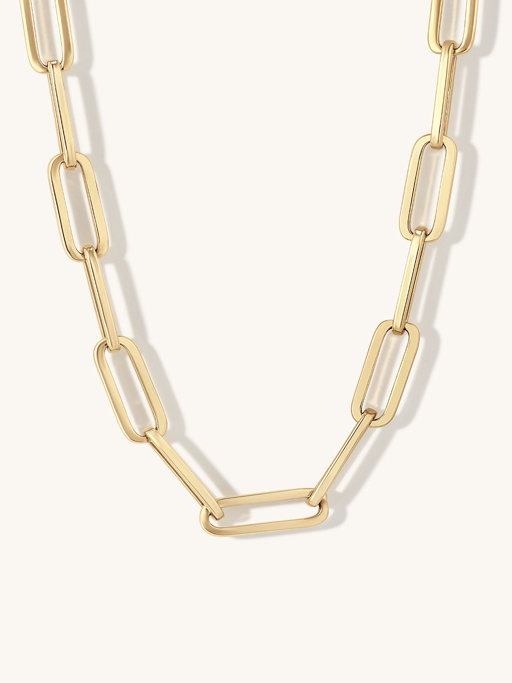 A gold paperclip chain necklace with large, polished oval links, displayed against a clean off-white background.