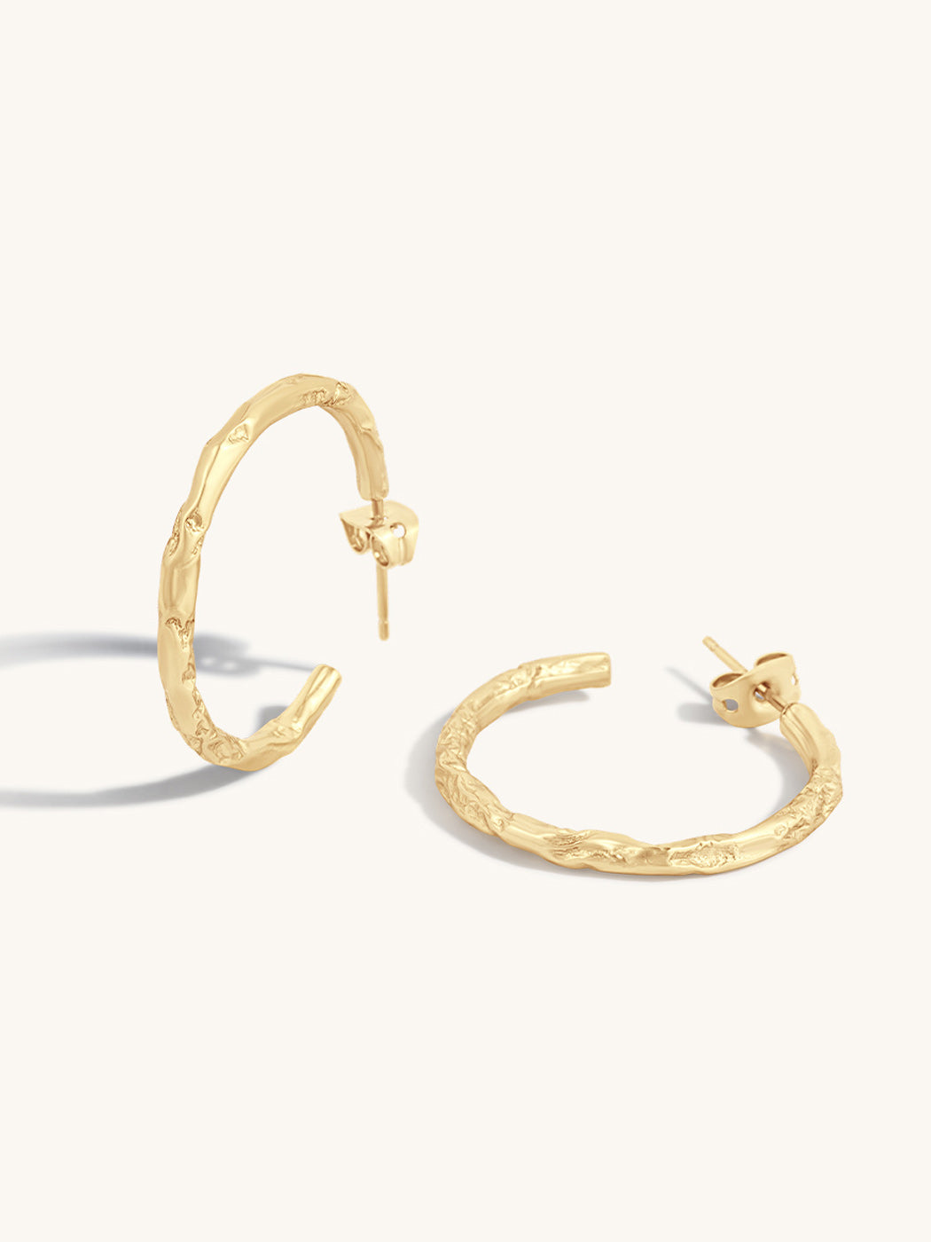 A pair of textured gold hoop earrings with post-back closures, displayed on a clean off-white background.