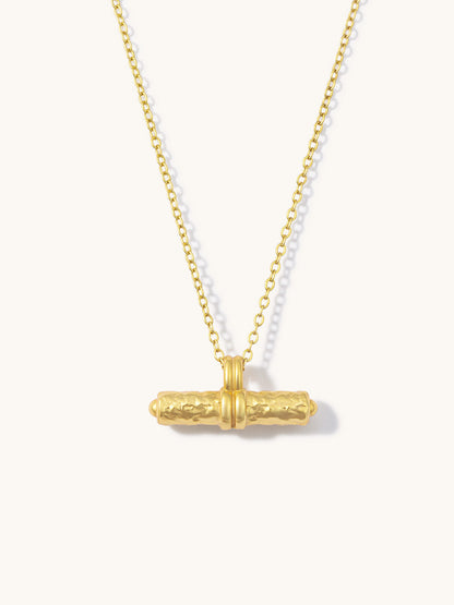 A gold chain necklace featuring a textured horizontal bar pendant, displayed against a clean off-white background.