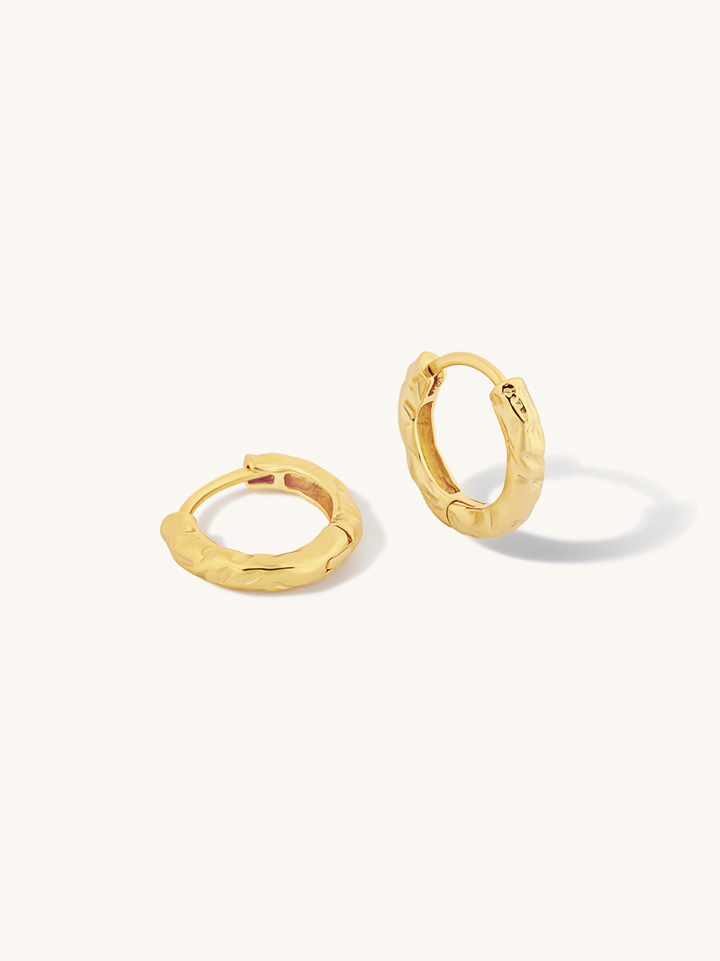 A pair of textured gold huggie hoop earrings on a clean, off-white background.
