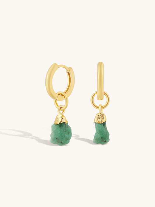 A pair of gold huggie hoop earrings with dangling raw green stone charms, displayed on a clean off-white background.